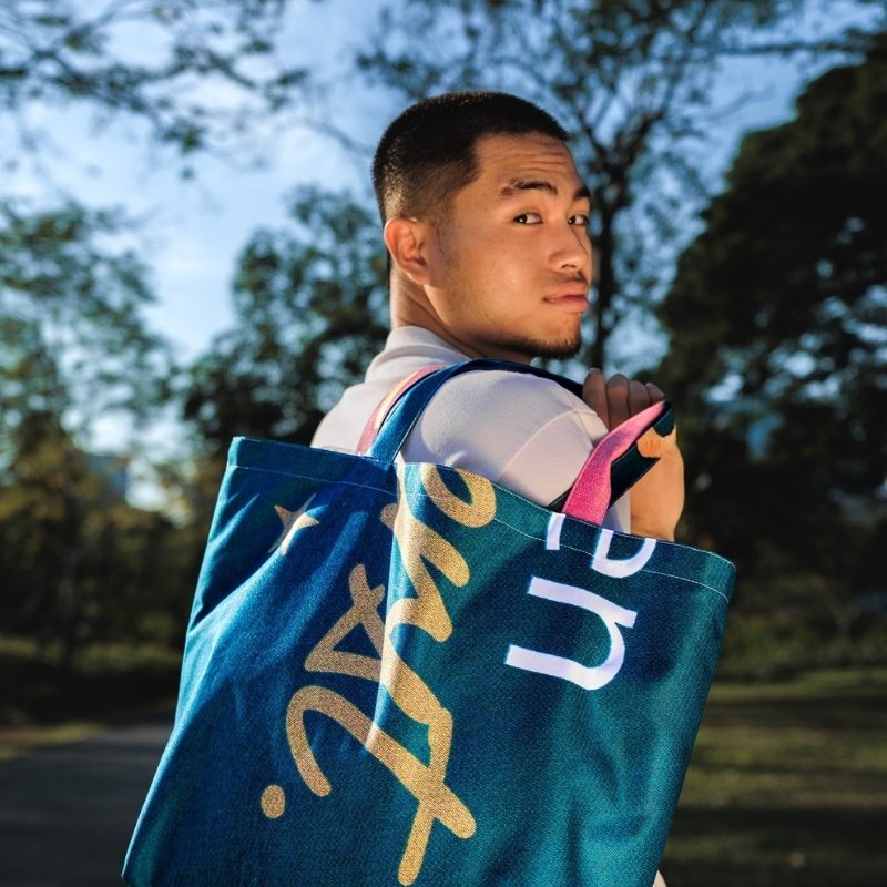 A person walk through a park with a vivid green Large Morph Tote on his shoulder.