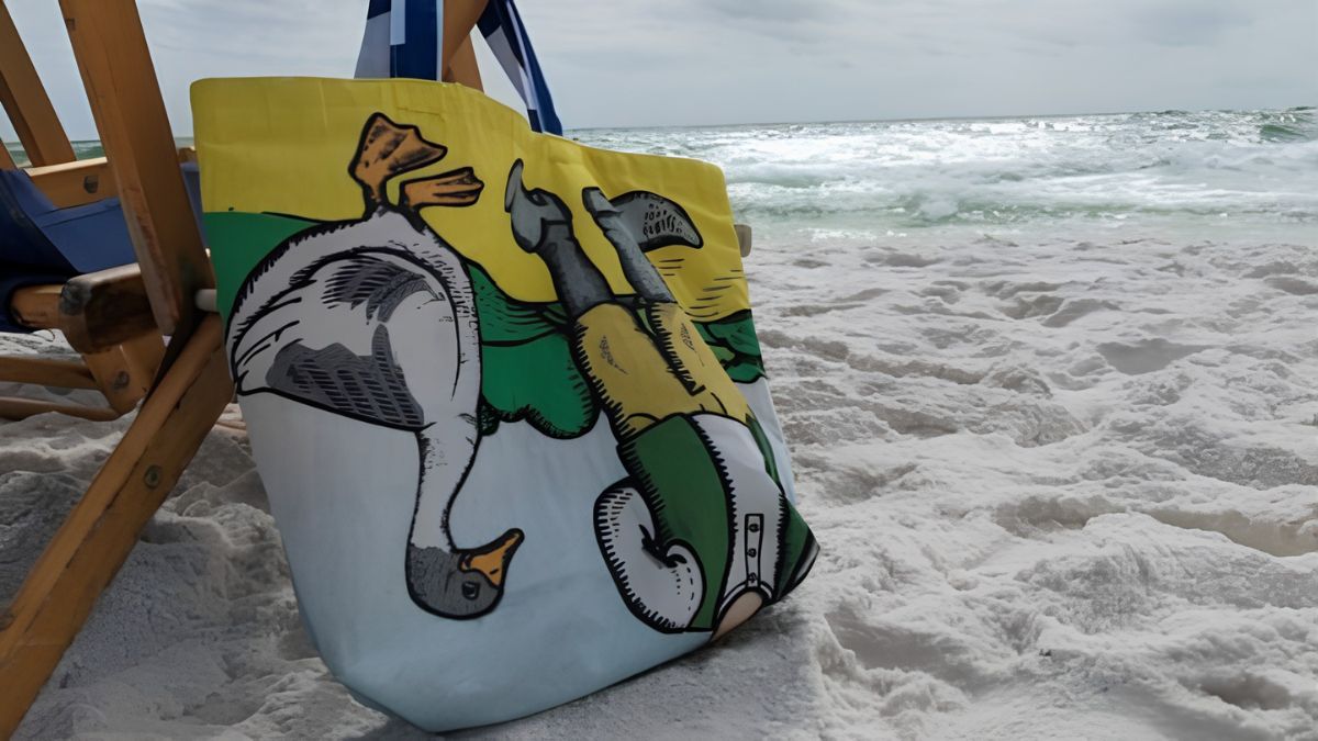 Colorful upcycled tote bag made from printed polyester banner offcuts by Morph Bags hangs on the arm of a lounge chair on the beach.