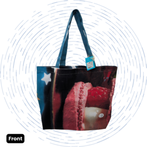 The front view of a one-of-a-kind dark Large Morph Tote featuring a pink macaron and berry graphic with a white star print and teal straps.