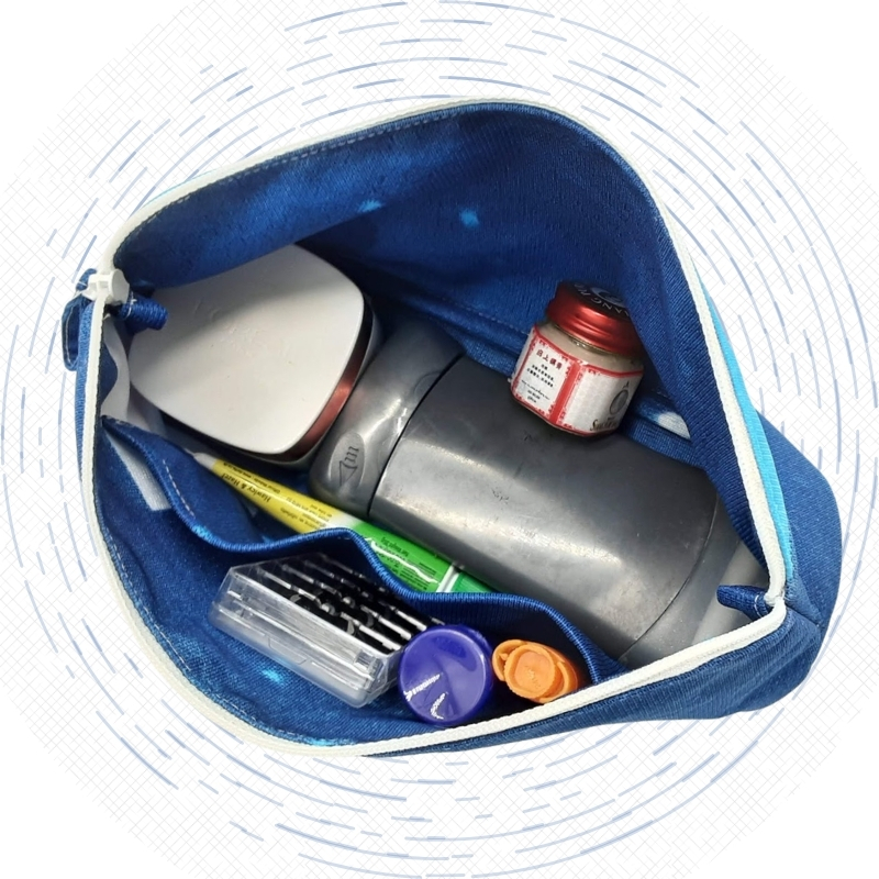 Inside of a blue upcycled Cosmetics Bag packed with travel toiletries, including a deodorant stick, facial cream, toothbrush, razor blades, lip balm, and a bottle of herbal ointment.