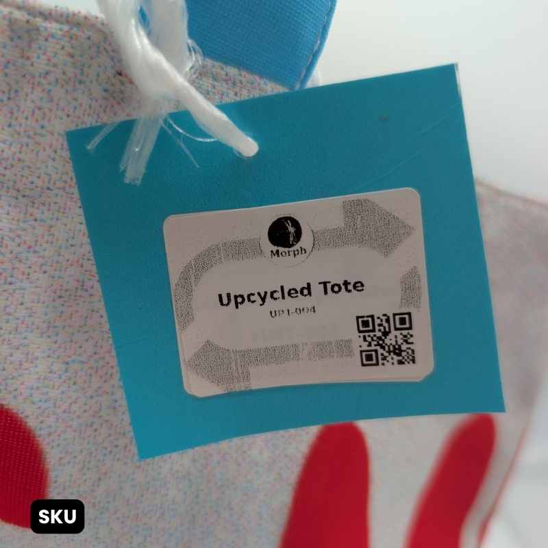 A closeup of the SKU of a white tote bag with bold red text and a brightly colored blue and red striped handle.